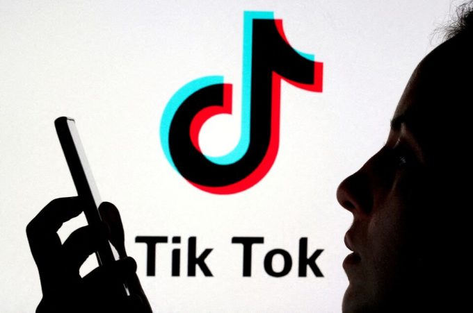 Một người sử dụng điện thoại di động trước logo TikTok.Ảnh: Reuters