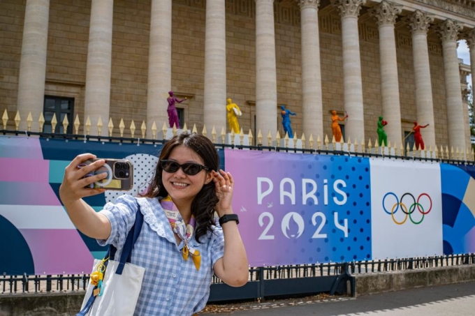 Nữ du khách tạo dáng trước tòa nhà Quốc hội ở Paris ngày 28/6, đằng sau tấm biểu ngữ có logo của Thế vận hội Olympic Paris 2024. Nguồn ảnh: Tân Hoa Xã